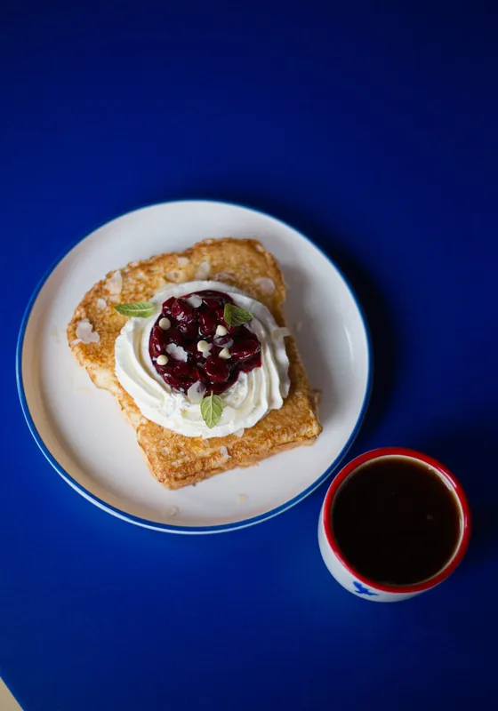 Pastry with cream and berries next to a cup of coffee on a blue table